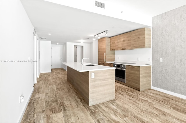 kitchen with stainless steel oven, modern cabinets, light wood-style floors, and visible vents