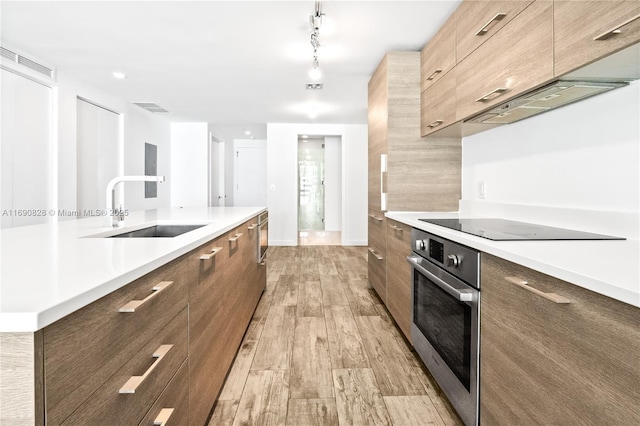 kitchen featuring stainless steel oven, modern cabinets, a sink, and black electric cooktop