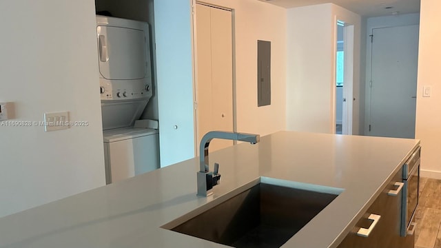 kitchen with stacked washer and dryer, hardwood / wood-style flooring, electric panel, and sink