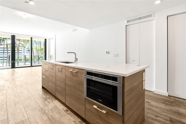 kitchen with oven, visible vents, modern cabinets, a sink, and light wood-style floors