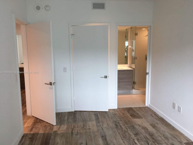 unfurnished bedroom featuring ensuite bathroom and dark hardwood / wood-style flooring