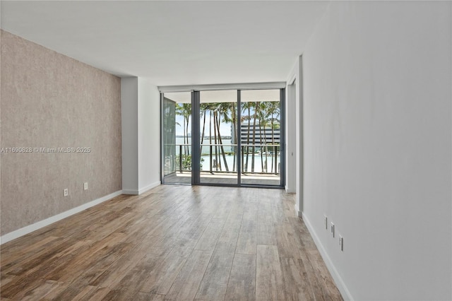 empty room featuring baseboards, wood finished floors, and a wall of windows