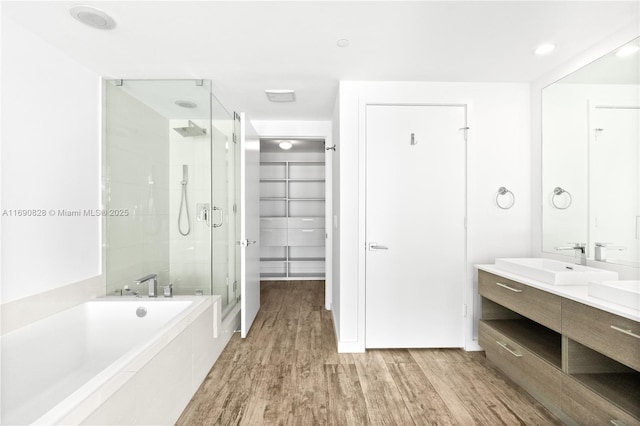 bathroom featuring a shower stall, wood finished floors, a sink, a walk in closet, and a garden tub