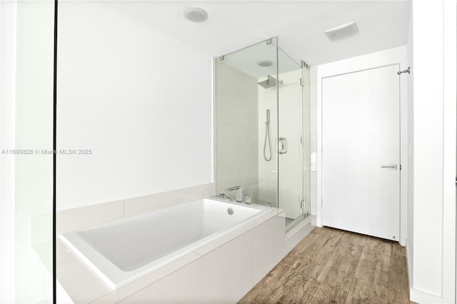 bathroom with a bath, wood finished floors, and a stall shower