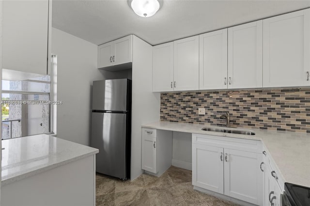 kitchen with white cabinetry, stainless steel refrigerator, light stone countertops, decorative backsplash, and sink