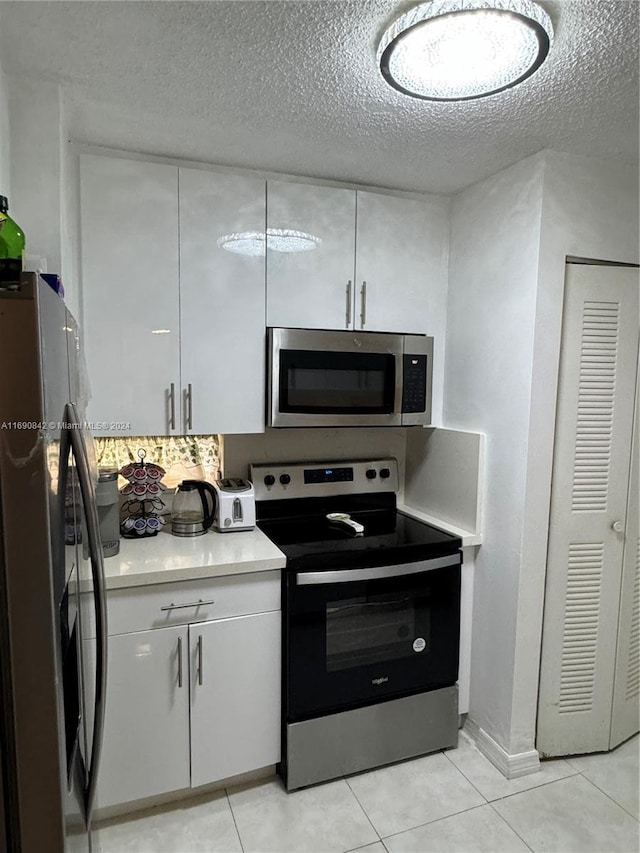 kitchen with white cabinetry, stainless steel appliances, a textured ceiling, and light tile patterned flooring