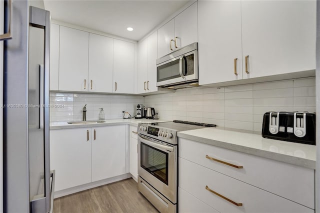 kitchen with stainless steel appliances, sink, tasteful backsplash, white cabinets, and light wood-type flooring