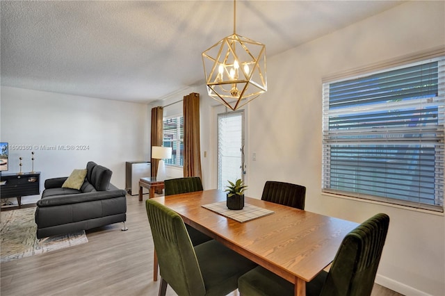 dining room with light wood-type flooring, a textured ceiling, and a notable chandelier