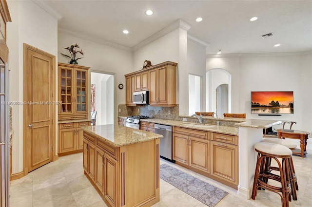 kitchen with stainless steel appliances, a kitchen breakfast bar, light stone countertops, crown molding, and a center island