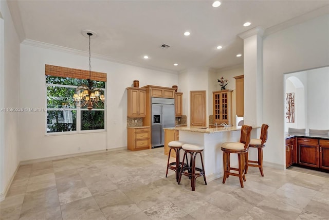 kitchen with a breakfast bar, kitchen peninsula, crown molding, light stone countertops, and stainless steel built in refrigerator