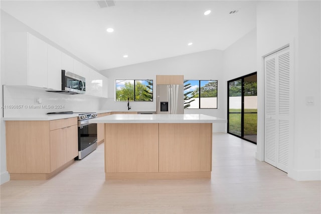 kitchen featuring a kitchen island, lofted ceiling, stainless steel appliances, and white cabinets