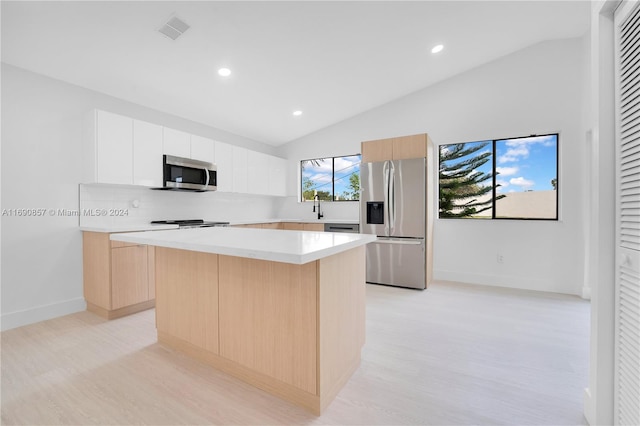 kitchen with a center island, white cabinetry, appliances with stainless steel finishes, lofted ceiling, and light hardwood / wood-style flooring