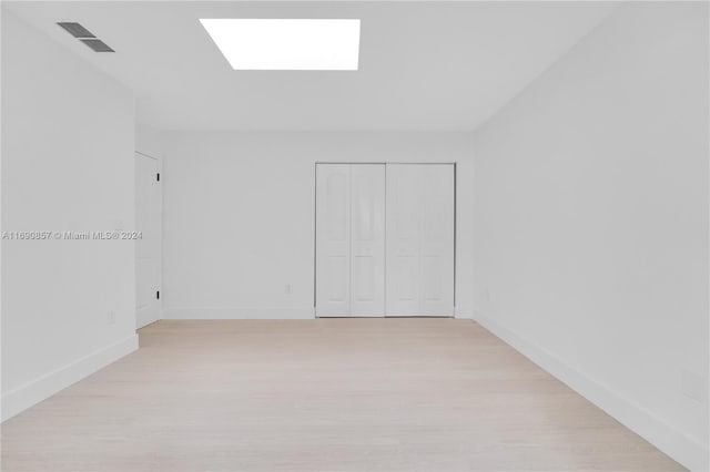 empty room with a skylight and light hardwood / wood-style flooring