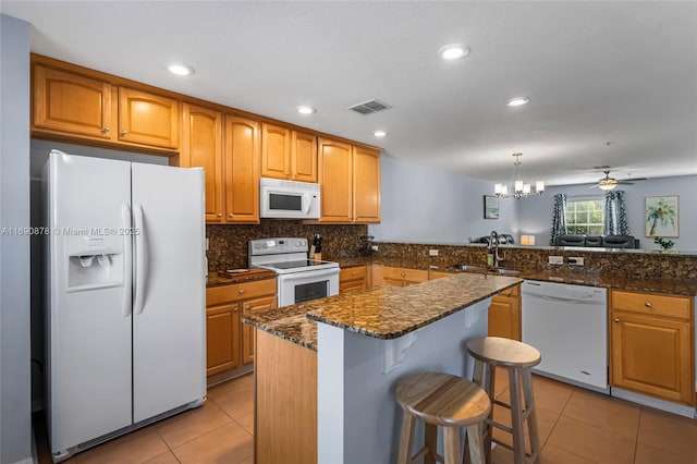 kitchen with white appliances, dark stone counters, hanging light fixtures, ceiling fan with notable chandelier, and sink