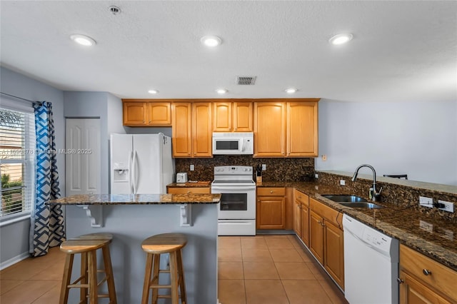 kitchen with white appliances, dark stone counters, sink, a breakfast bar, and light tile patterned floors