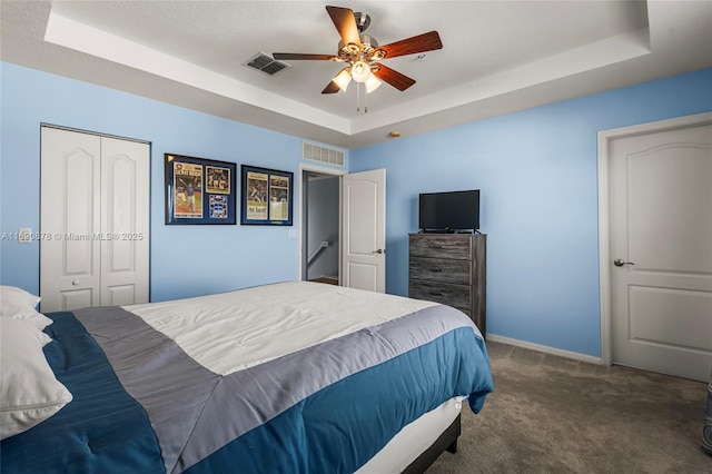 bedroom with ceiling fan, a tray ceiling, and dark colored carpet