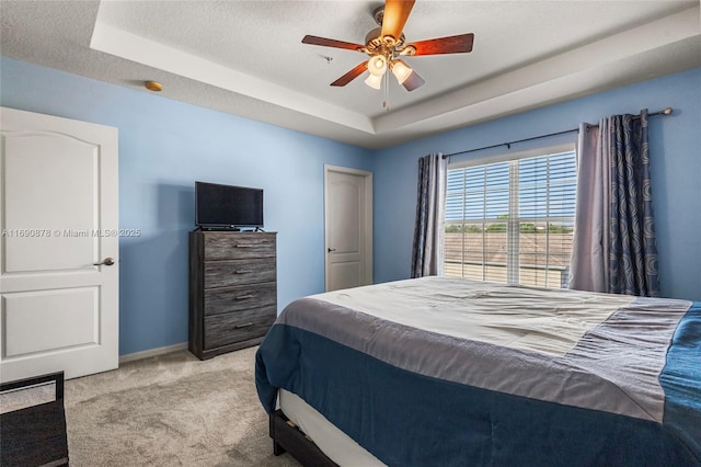 carpeted bedroom with ceiling fan, a tray ceiling, and a textured ceiling