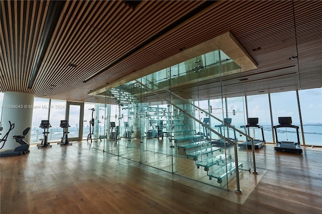 exercise room featuring hardwood / wood-style floors, a water view, and floor to ceiling windows