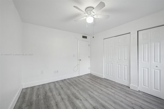 unfurnished bedroom featuring multiple closets, light hardwood / wood-style floors, and ceiling fan