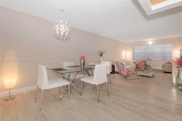 dining area featuring a chandelier, baseboards, a textured ceiling, and light wood-style flooring