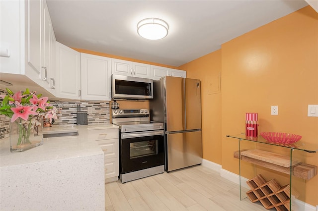 kitchen with light wood-type flooring, backsplash, white cabinetry, appliances with stainless steel finishes, and baseboards