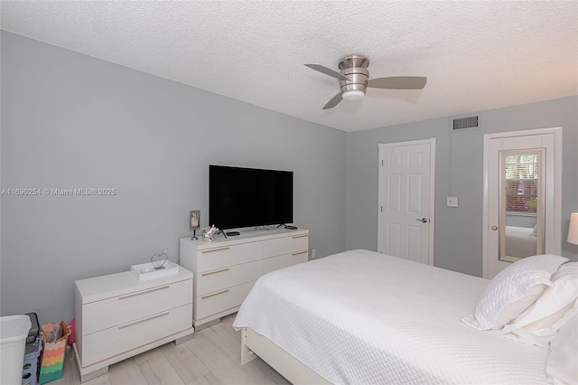 bedroom with visible vents, a textured ceiling, light wood-style floors, and a ceiling fan