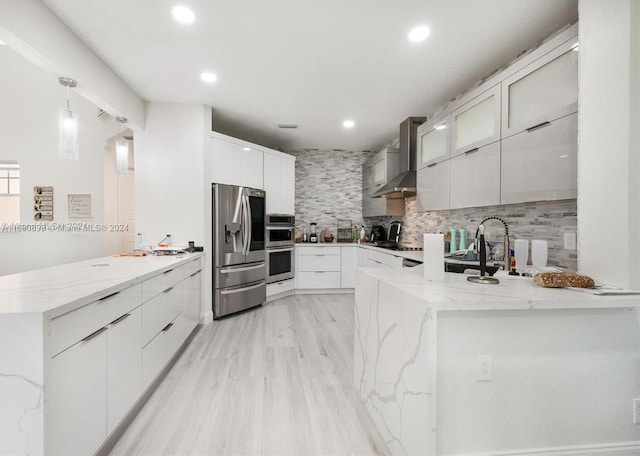 kitchen featuring white cabinetry, kitchen peninsula, appliances with stainless steel finishes, and wall chimney exhaust hood