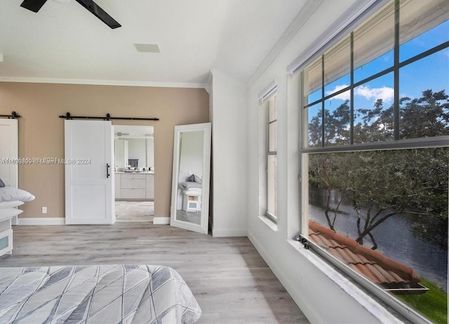 bedroom with a barn door, ceiling fan, light hardwood / wood-style flooring, and ornamental molding