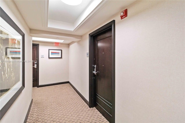 hallway with light colored carpet and a tray ceiling