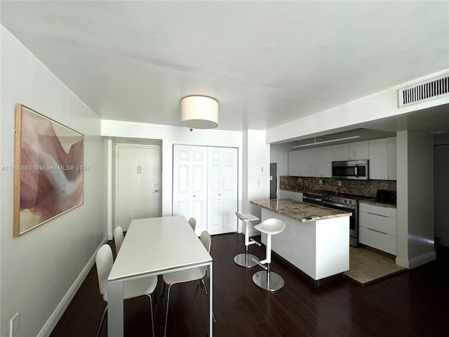 kitchen featuring stainless steel appliances, dark stone counters, decorative backsplash, white cabinets, and dark wood-type flooring