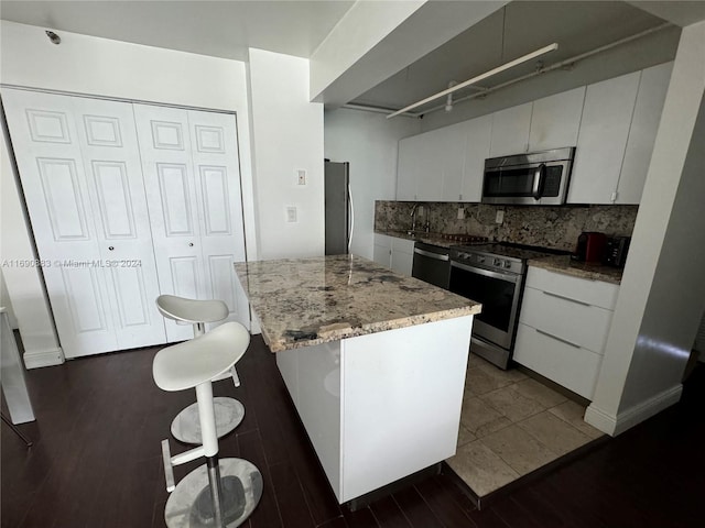 kitchen featuring dark wood-type flooring, white cabinets, a kitchen bar, and stainless steel appliances