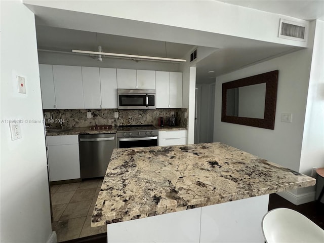 kitchen featuring white cabinetry, appliances with stainless steel finishes, tasteful backsplash, a kitchen breakfast bar, and light tile patterned floors