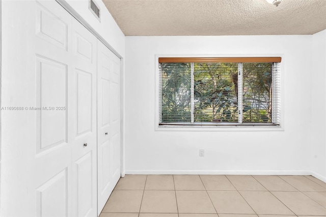 unfurnished bedroom featuring a textured ceiling, light tile patterned floors, visible vents, baseboards, and a closet