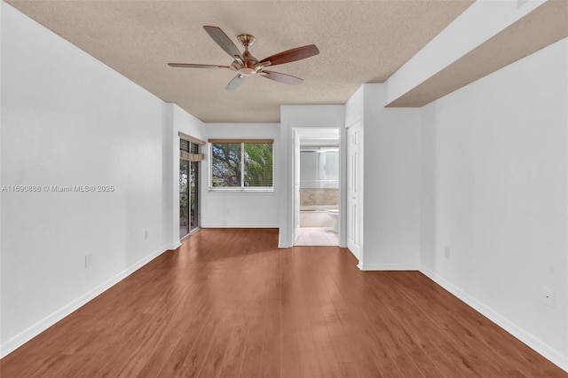 spare room with ceiling fan, a textured ceiling, baseboards, and dark wood-type flooring