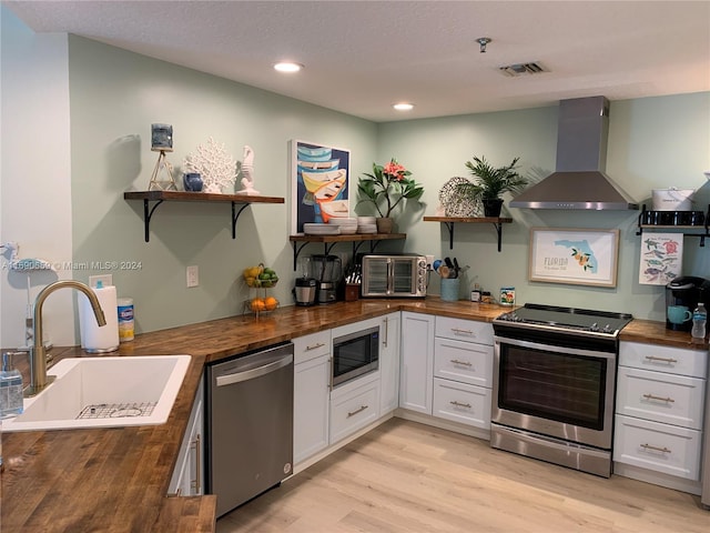 kitchen with white cabinets, stainless steel appliances, butcher block countertops, and wall chimney exhaust hood