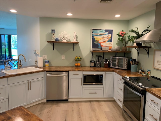 kitchen featuring stainless steel appliances, butcher block counters, white cabinetry, sink, and island exhaust hood