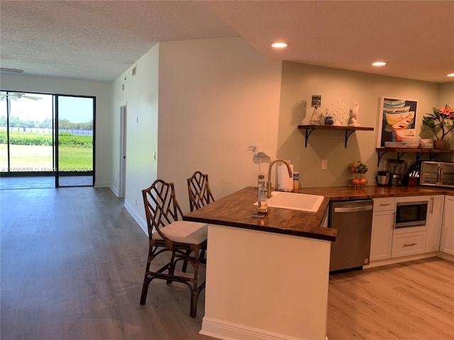 kitchen with white cabinetry, appliances with stainless steel finishes, sink, kitchen peninsula, and light hardwood / wood-style flooring