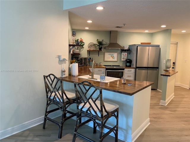 kitchen featuring stainless steel appliances, kitchen peninsula, a breakfast bar area, ventilation hood, and light wood-type flooring