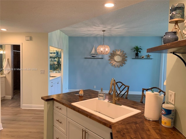 kitchen featuring butcher block countertops, white cabinetry, decorative light fixtures, sink, and light hardwood / wood-style flooring