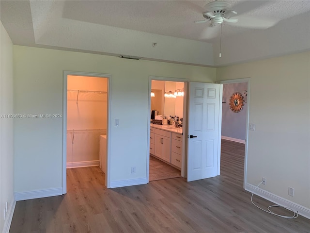 unfurnished bedroom with a textured ceiling, ceiling fan, a closet, light wood-type flooring, and a walk in closet