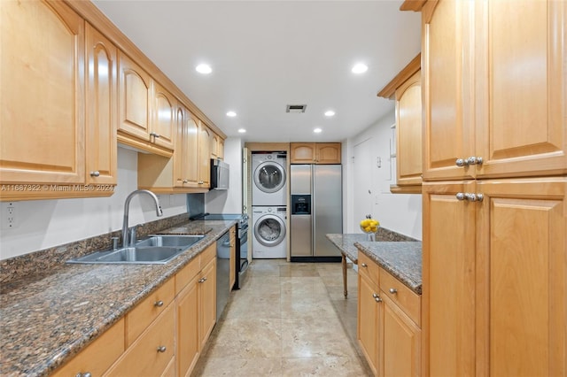 kitchen with stacked washer and dryer, appliances with stainless steel finishes, sink, and dark stone countertops