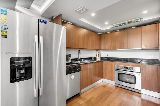 kitchen with sink, appliances with stainless steel finishes, a tray ceiling, light hardwood / wood-style floors, and exhaust hood