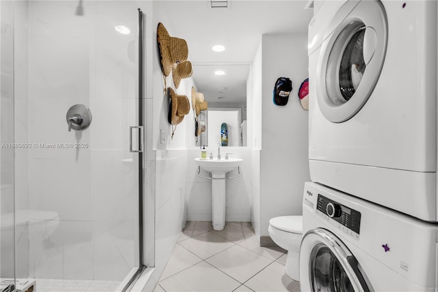 bathroom featuring stacked washer / dryer, a shower with door, tile patterned floors, and toilet