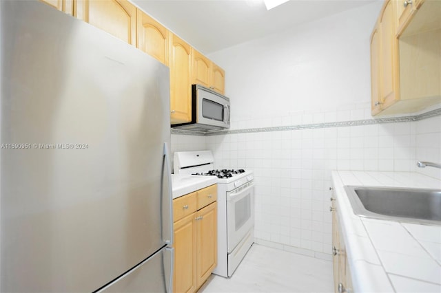 kitchen featuring tile walls, light brown cabinets, appliances with stainless steel finishes, and sink