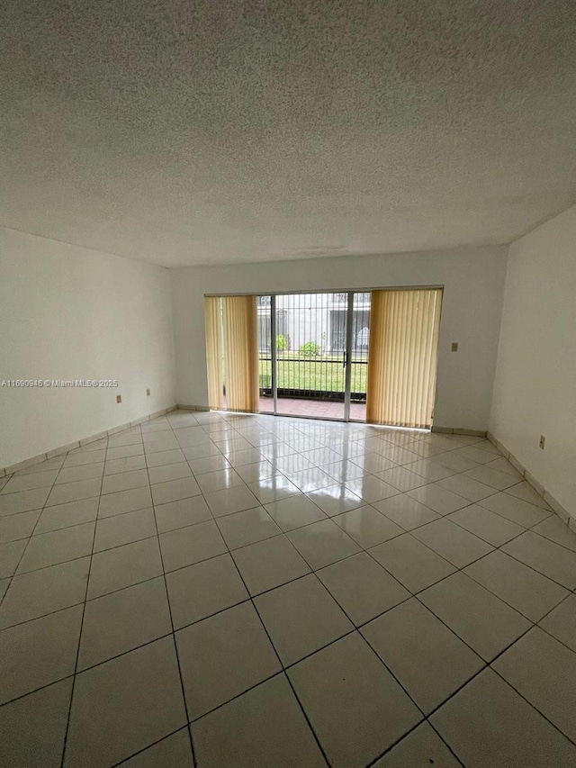 spare room featuring light tile patterned floors, baseboards, and a textured ceiling