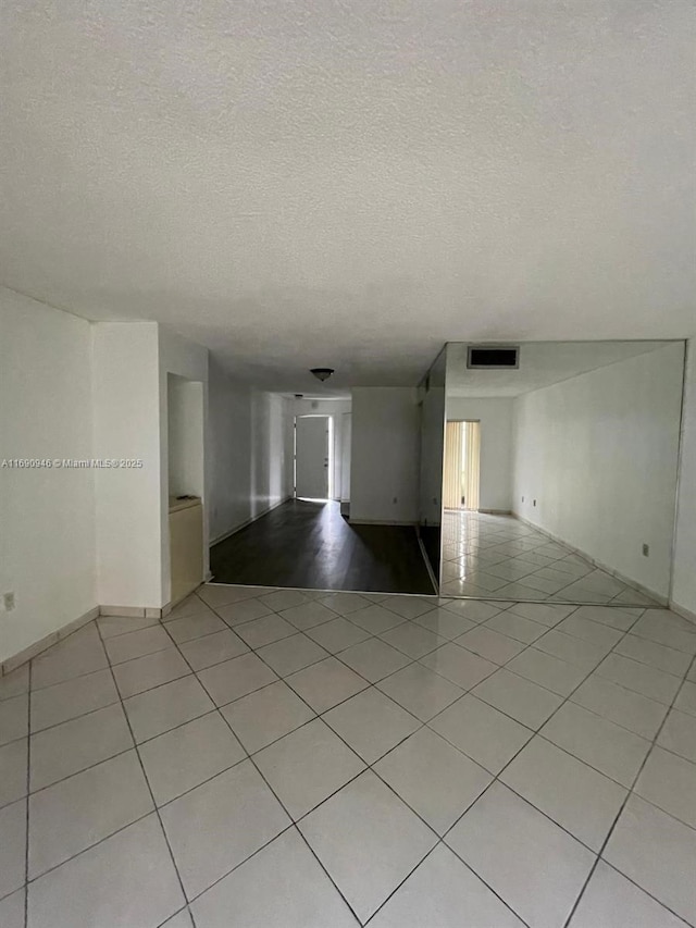 unfurnished room with light tile patterned flooring, a textured ceiling, and visible vents
