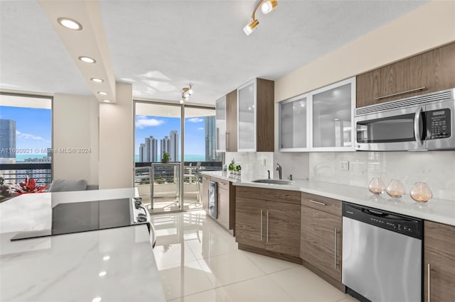 kitchen with stainless steel appliances, backsplash, light tile patterned floors, expansive windows, and sink