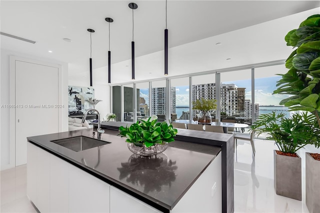 kitchen featuring sink, light tile patterned flooring, dark stone countertops, decorative light fixtures, and white cabinets