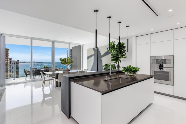 kitchen with stainless steel double oven, sink, decorative light fixtures, a water view, and white cabinets