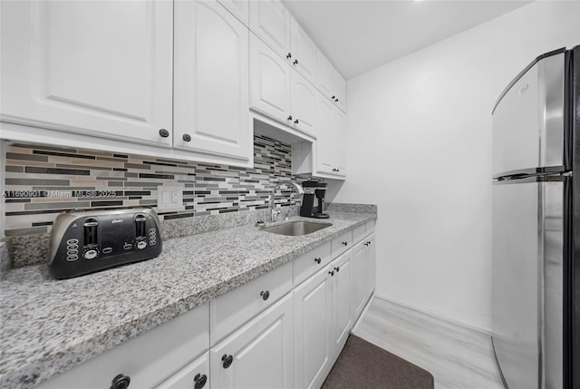 kitchen featuring sink, light stone counters, stainless steel fridge, decorative backsplash, and white cabinets